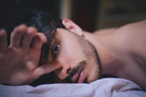 Man in bed managing constant arousal alone