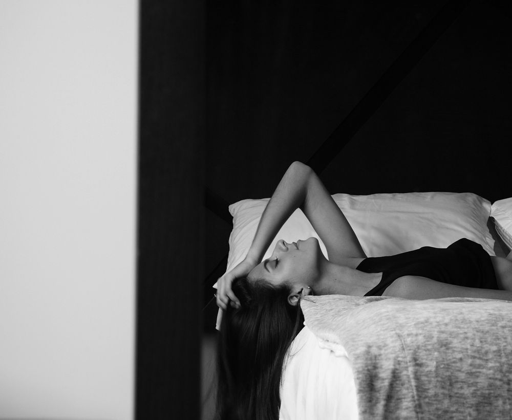 Woman lying back on white bed enjoying intimate moment with her escort companion
