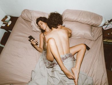 Woman checking her phone in bed during a moment of intimacy