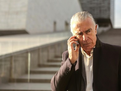 Elderly man walking on street, talking on phone to escort.