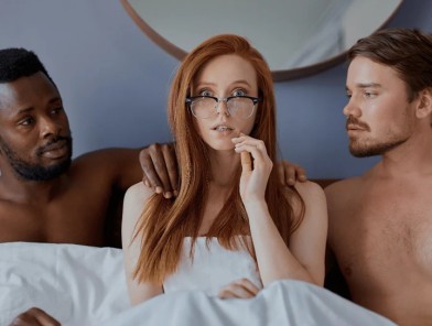 Female escort smiling with couple in bed