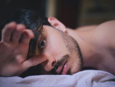Man in bed managing constant arousal alone