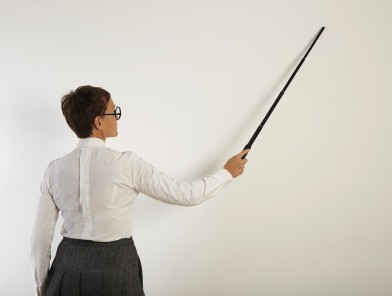 A female teacher standing sternly at her desk.