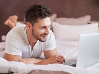 Man browsing online content on a laptop from his bedroom